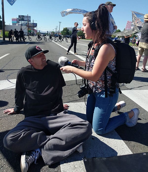 Student Karina Gonzalez interviews a person sitting on the ground.