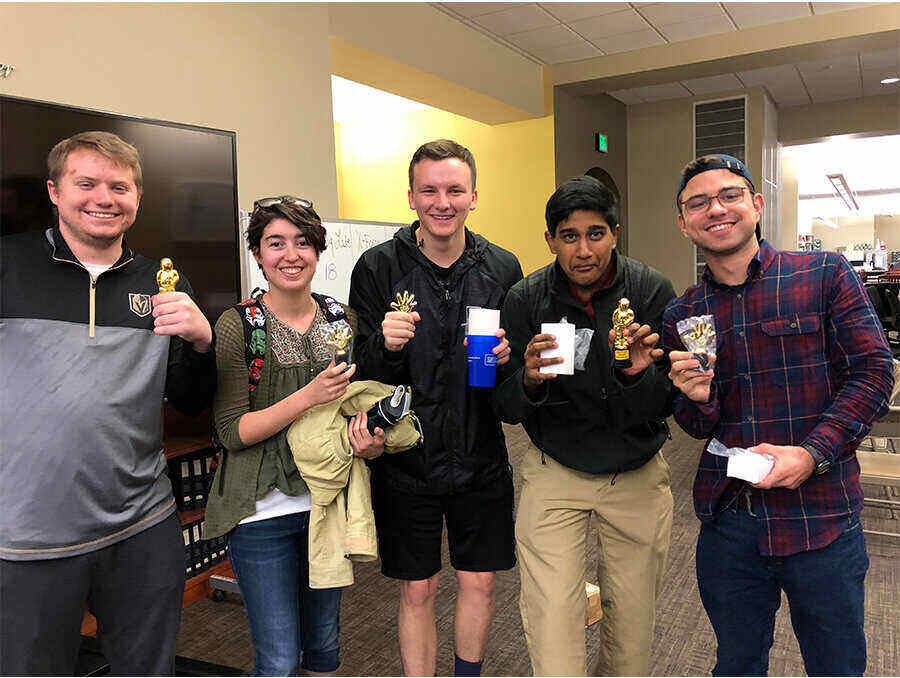 A mixed gender, five- person Trivia Night team poses for a photo with their Trivia Night prizes.