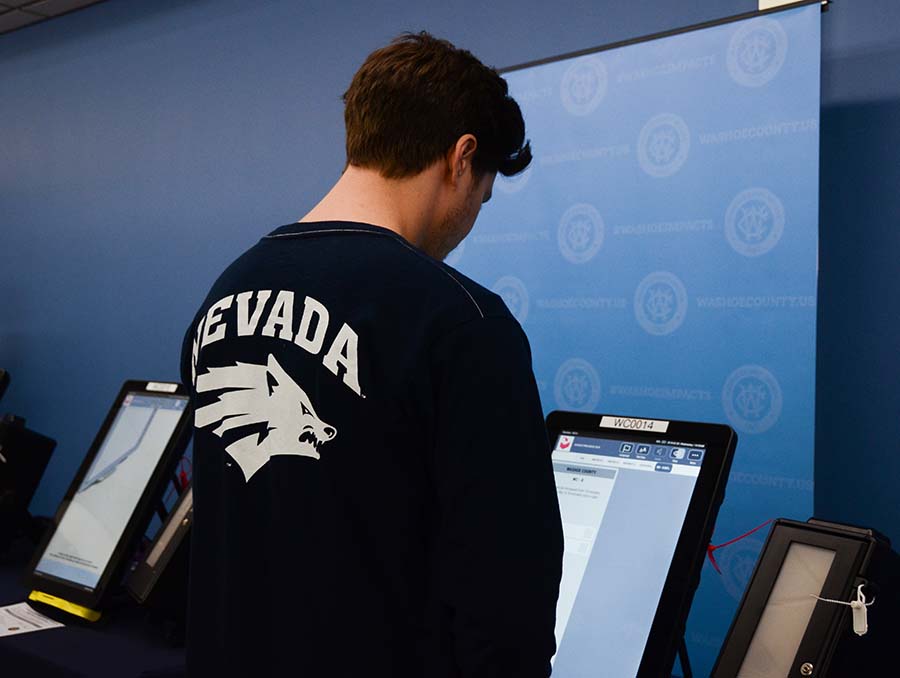 Person with a Nevada Wolf Pack shirt on stands in front of a voting machine.