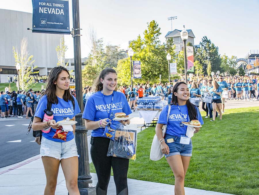 Students in blue shirts with food plates in hand walk through the Gateway plaza on the University of Nevada, Reno campus.