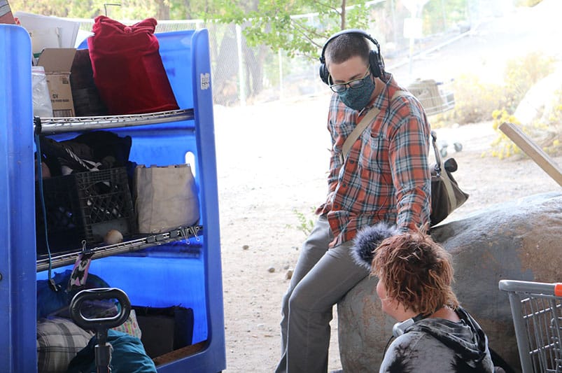 A student interviews a person sitting on the ground outside.