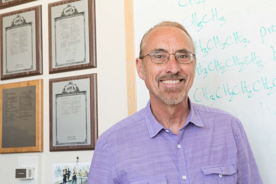 Tom Bell stands in front of a whiteboard. 