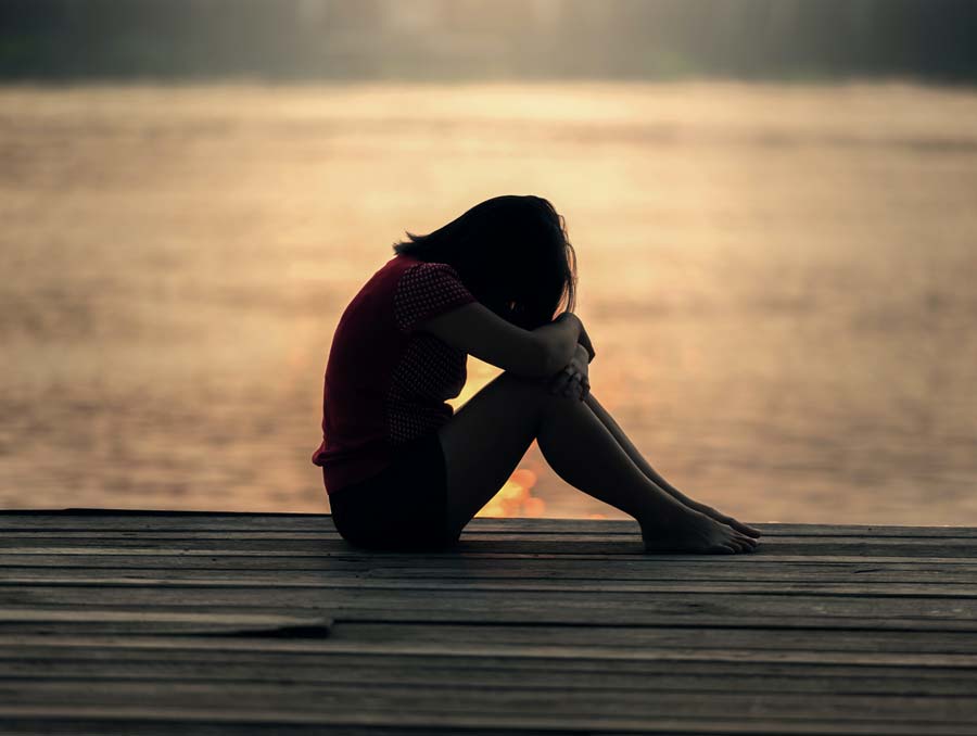 Silhouette of girl on a dock resting her forehead on her knees.