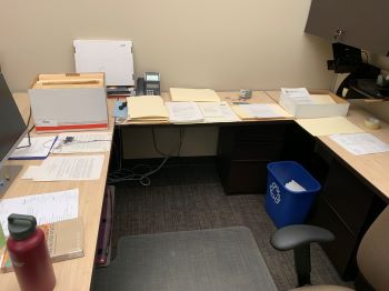 Three tables in a U-shape, covered in small tidy stacks of papers. 