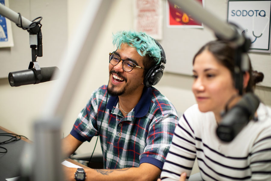 Two students sit in an audio recording studio recording a podcast