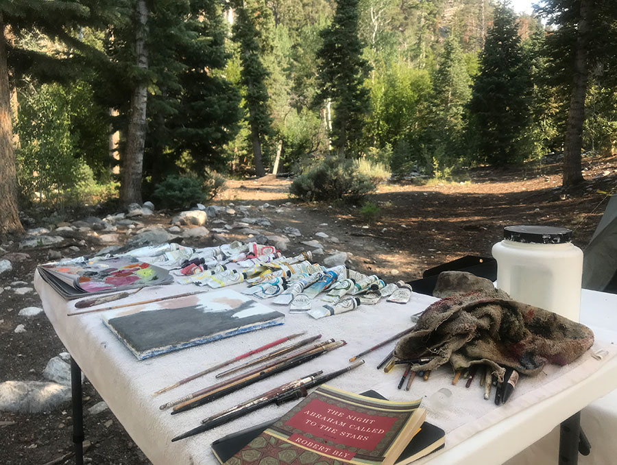 Artist table with paint, brushes and canvas outside in campground