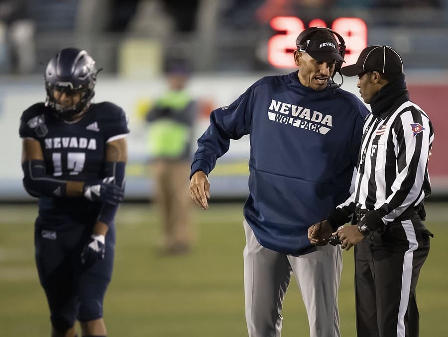 Coach Jay Norvell talking to a referee at Wolf Pack football game, a player and a game official can be seen in the background