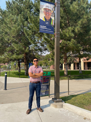 Huynh stands smiling under his Wolf Pack Way banner on campus outside of the William Raggio building.
