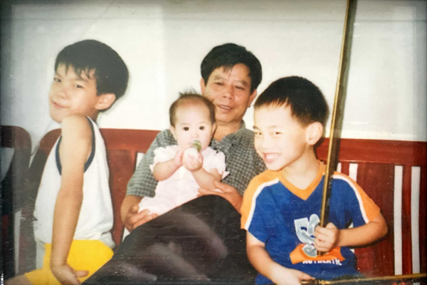 An older man holds a baby with two younger children on either side.