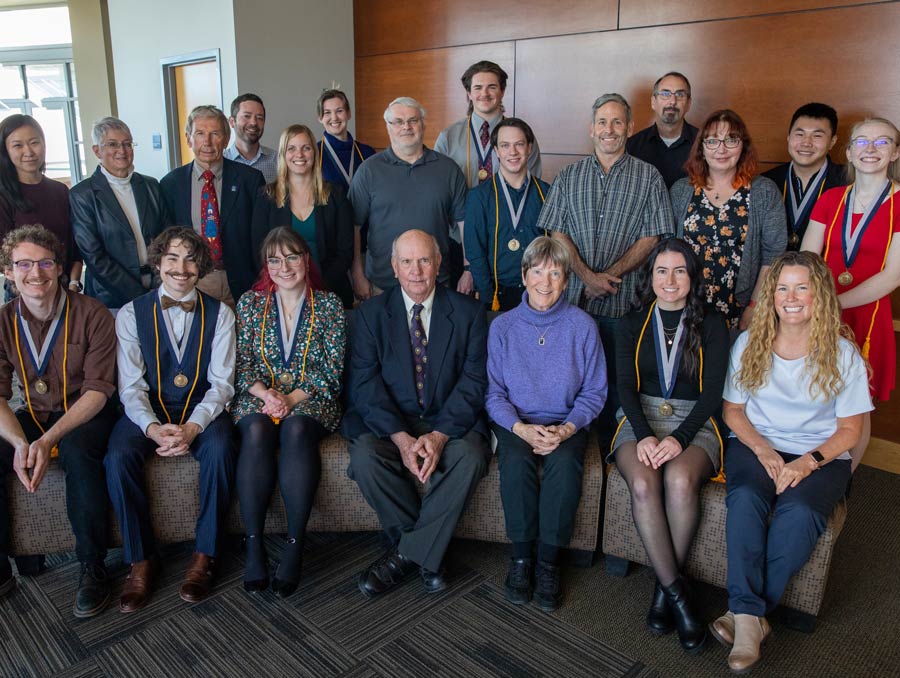 People sit and stand in two rows, smiling for a photo.