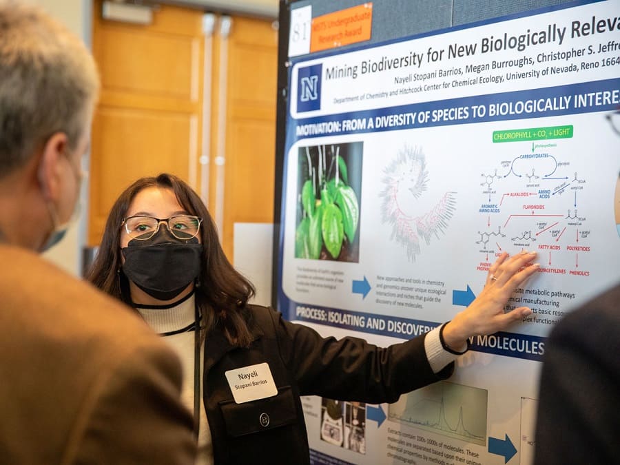 A student presents their poster to onlookers.