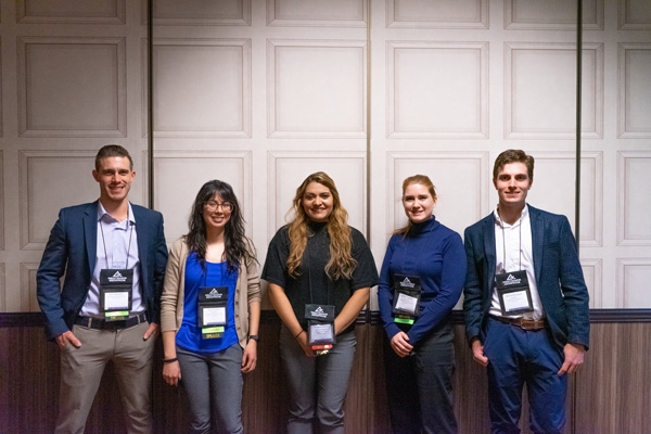 Five people stand with their conference badges in front of a paneled wall.