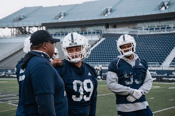 Dean Coach easton-Brooks talking with football players on the field at Mackay Stadium