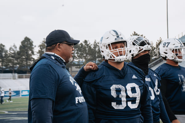 Dean Coach easton-Brooks talking with football players on the field at Mackay Stadium