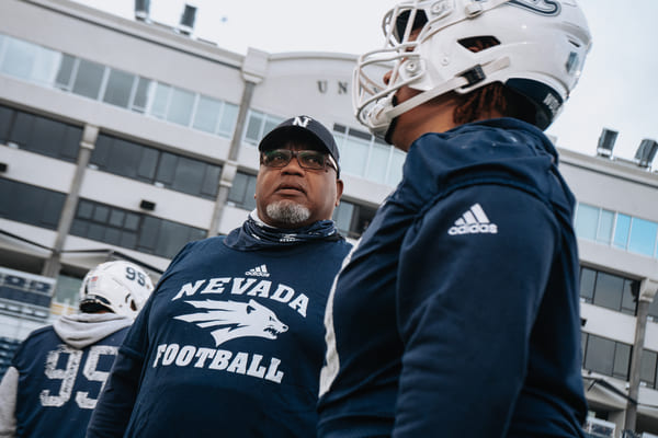 Dean Coach easton-Brooks talking with football players on the field at Mackay Stadium