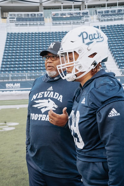 Dean Coach easton-Brooks talking with football players on the field at Mackay Stadium