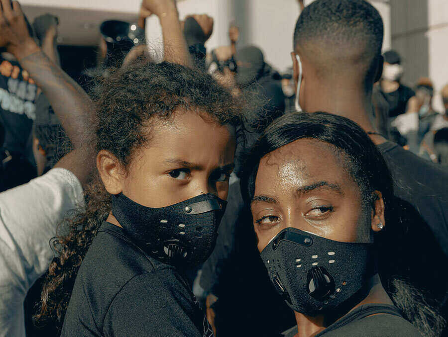 African-American woman holds a child, both wearing face coverings, at the George Floyd protests June 2, 2020, Charlotte, NC. Image courtesy of Unsplash.com