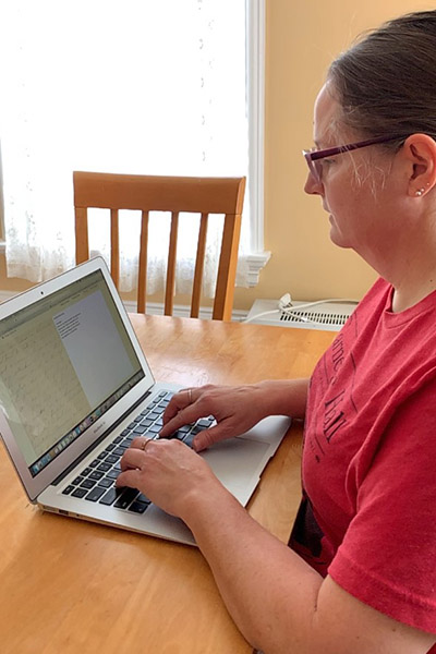 a woman with glasses sitting at a table working on a laptop