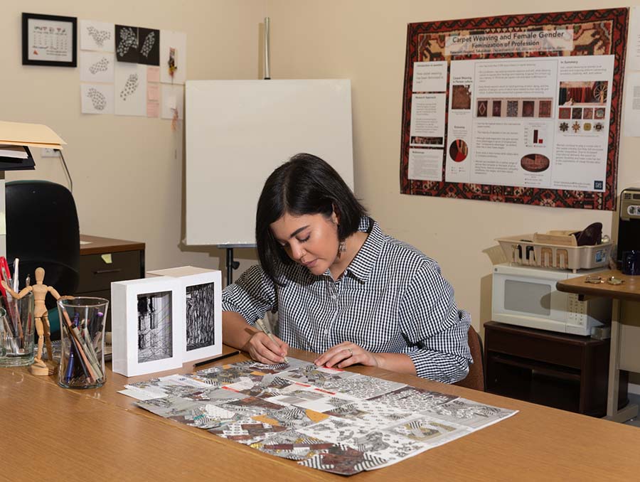 MFA student Sogand Tabatabaei sits at a desk working on a drawing. 