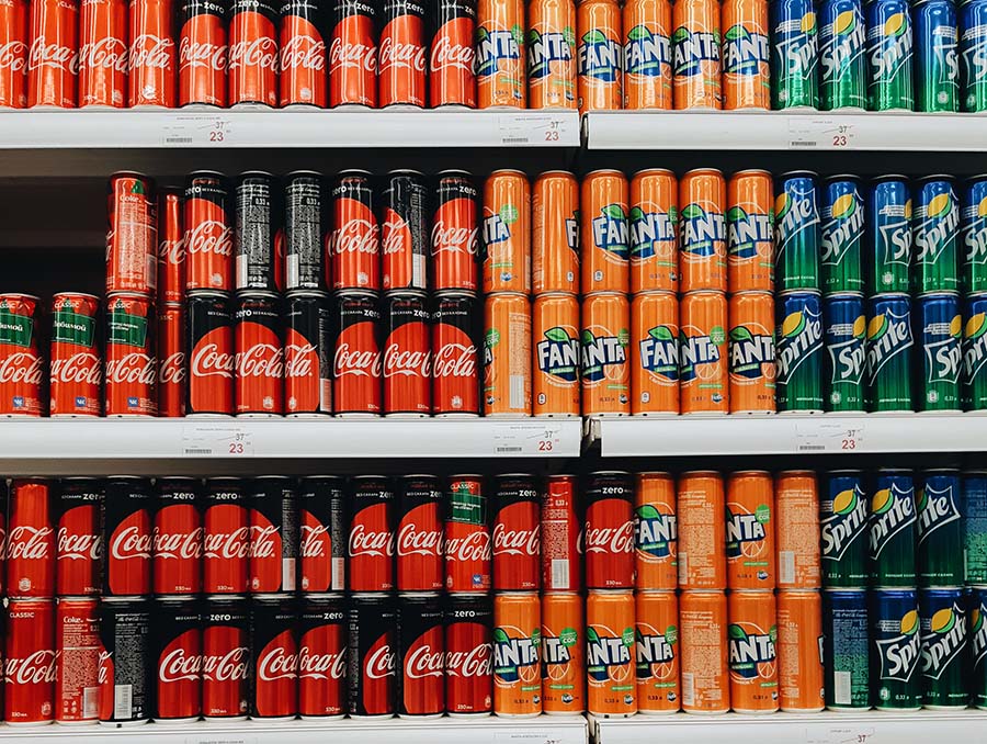 Grocery store shelves stocked with varying flavors and colors of soda cans. 