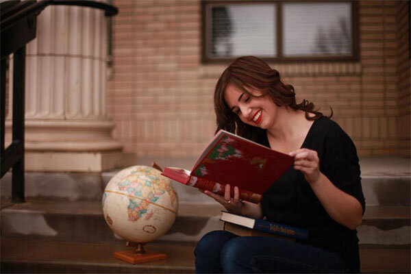 Young woman sitting and reading a book with a red cover.