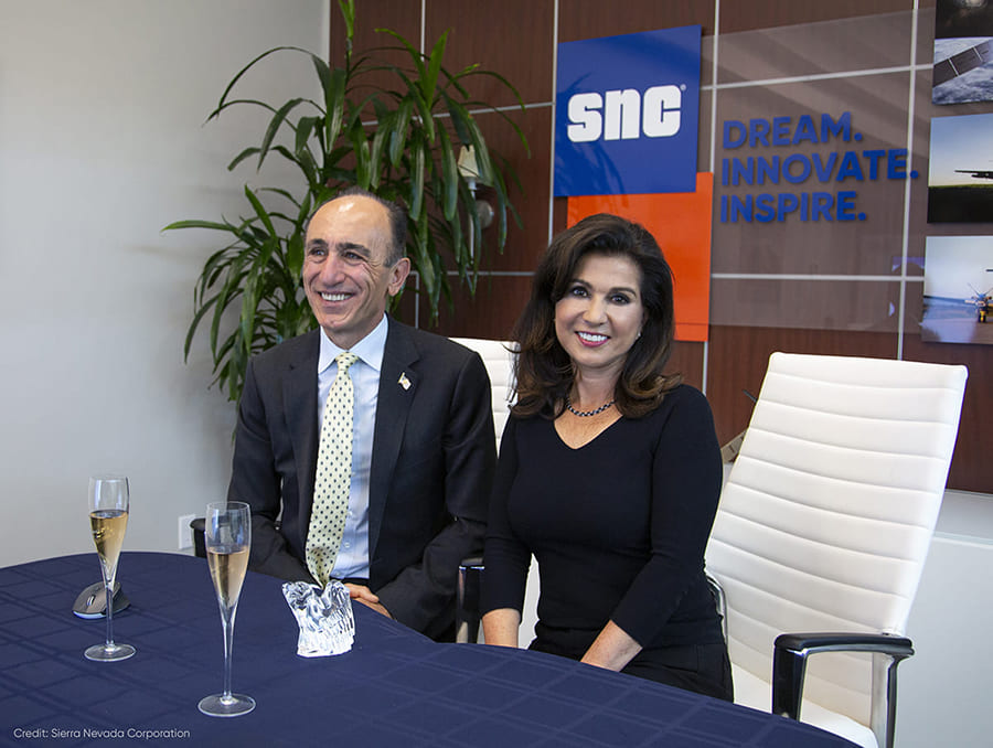 Two people seated at table with SNC banner in background