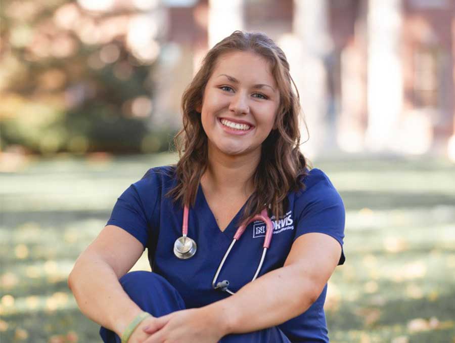 Haley Carroll sit in grass with nursing student uniform on