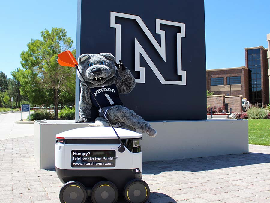 University of Nevada, Reno mascot Wolfie sits on the campus' N statue with a Starship food delivery robot at his feet