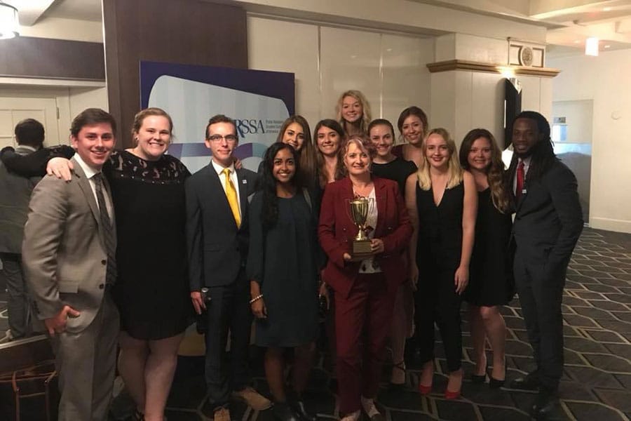 Alison Gaulden poses while holding a trophy with journalism students on both sides of her in a hallway at a convention center.