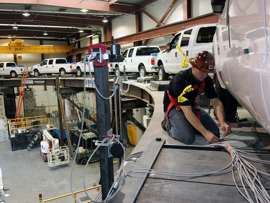 Researcher in hard hat working on curved bridge test that featured several trucks