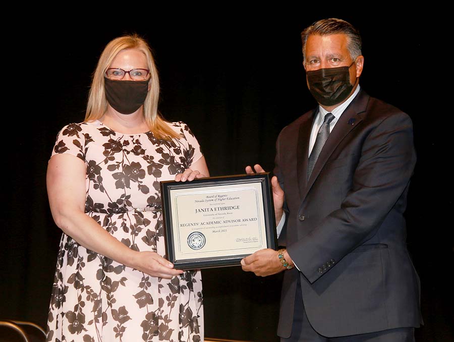 Janita Ethridge and Brian Sandoval pose for a photo, wearing masks, while holding a plaque.