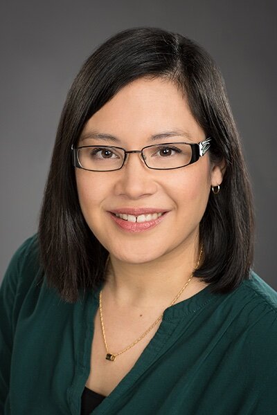 Lady with dark, short hair and glasses wearing a dark emerald green blouse