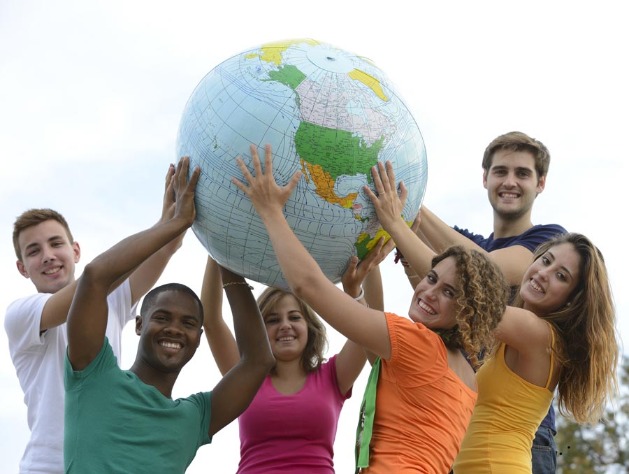 Diverse group of teenagers hold up an inflatable globe.