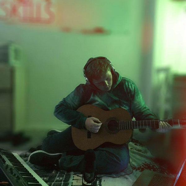 Andy Mills plays a guitar in a room.