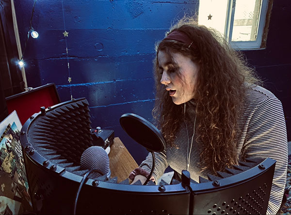 Vanessa Ribeiro sings into a microphone in a studio.