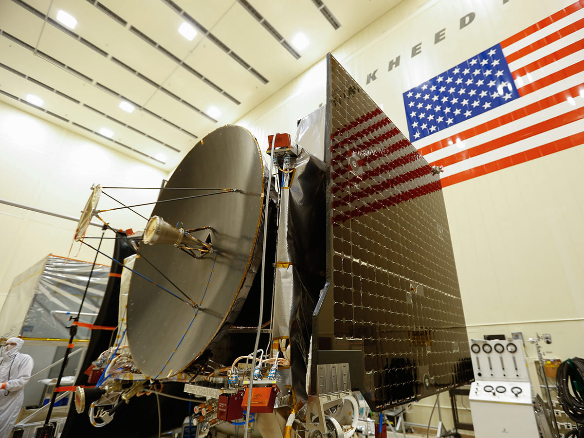 OSIRIS-REX in clean room-like environment with American flag in the background.