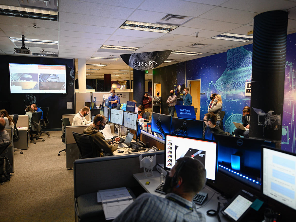 mission control room with computers and screen showing imagery from OSIRIS-REx.