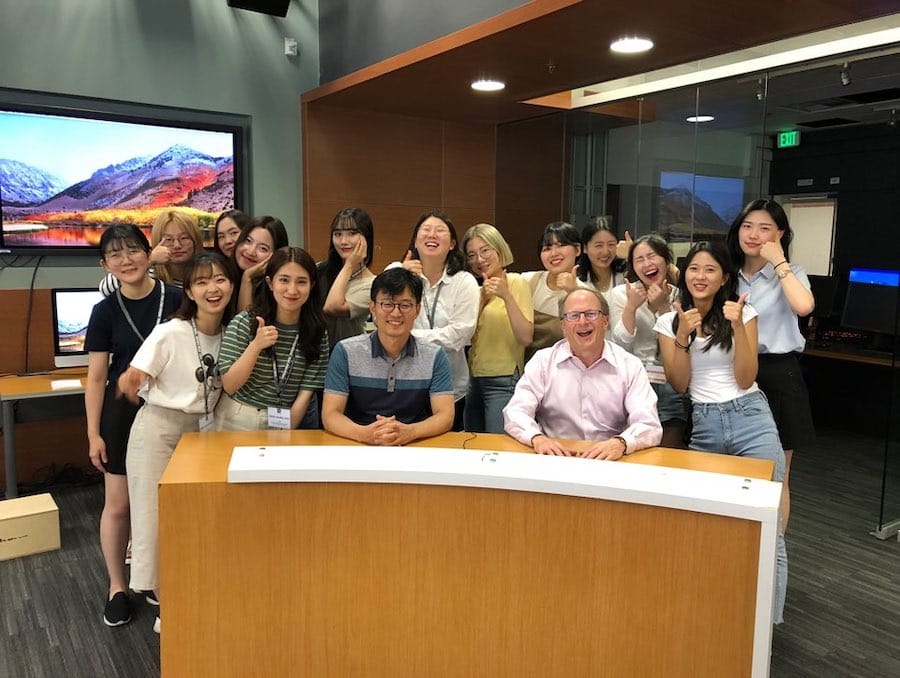 A group of South Korean students pose with Dean Stavitsky behind the anchor desk in the Reynolds Media Lab.