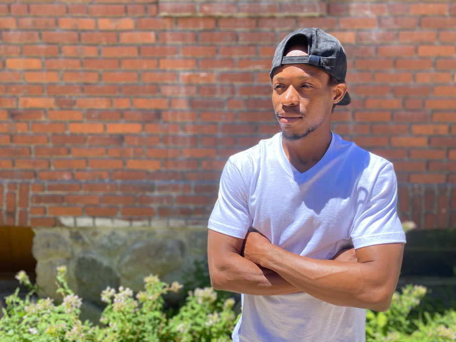 Photo of Blaize Abuntori with his arms crossed, standing in front of a brick wall posing for a photo.