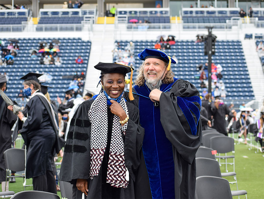 Judge Ari Tobi-Aiyemo stands next to Shawn Marsh in commencement attire on the field during graduation