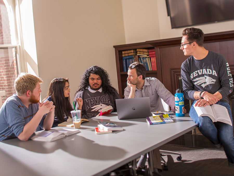 A group of students sitting around a table, talking. There are four males and a female.