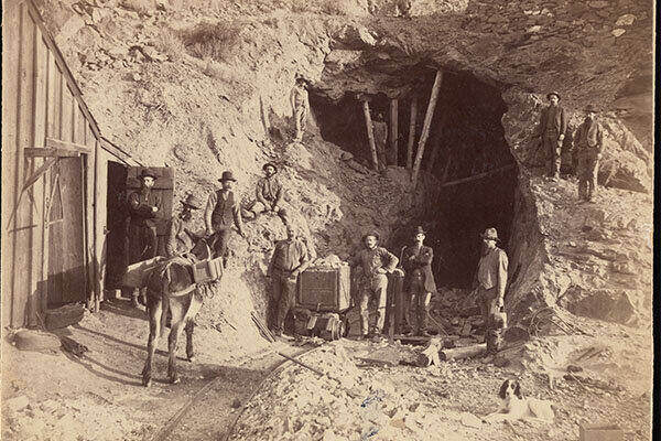 1880 photograph of miners posed with an ore cart, a dog, and a burro outside the entrance to a mine in Nevada