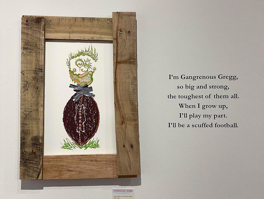 Art piece in wooden frame of a drawing of a football with a head coming out of it hangs on wall next to quote, “I’m Gangrenous Gregg, so big and strong, the toughest of them all. When I grow up, I’ll play my part. I’ll be a scuffed football.”