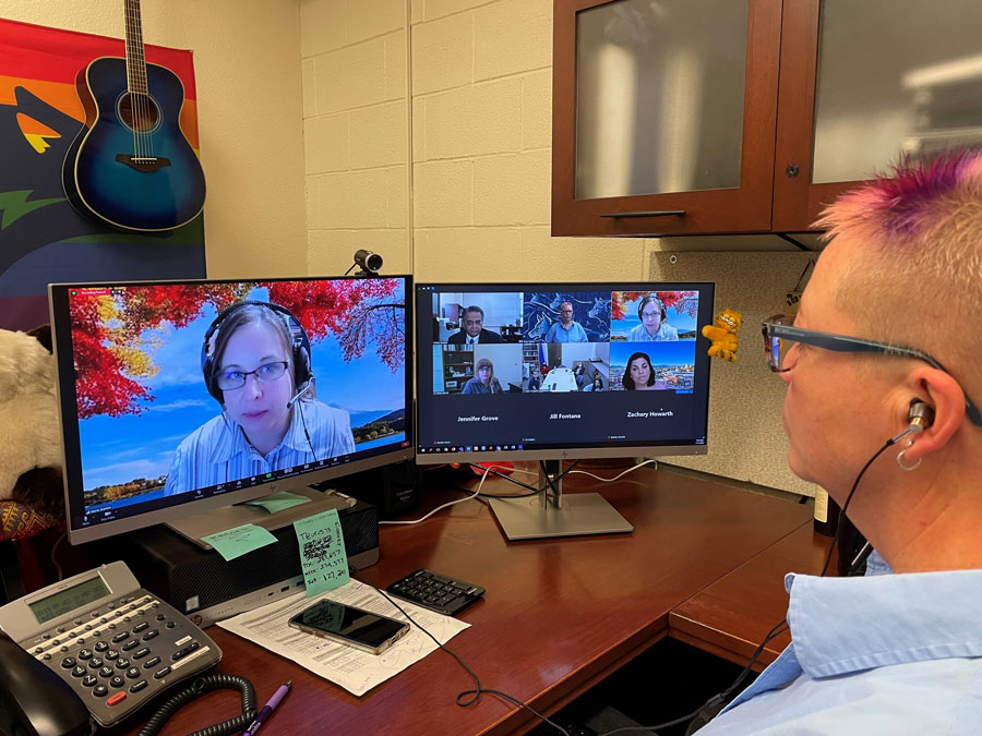 Erika Waday in front of monitors displaying a Zoom call.