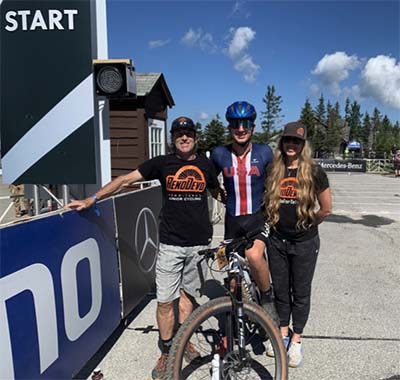 Luke Miers stands in the middle of two people while straddling his mountain bike