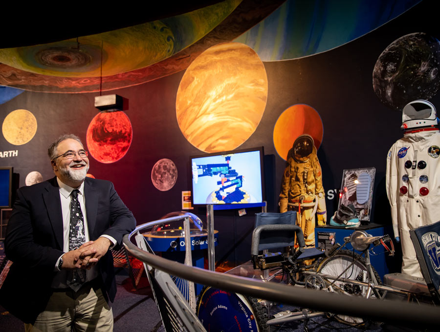 Planetarium Director Paul McFarlane stands on the left and is surrounded by space-related exhibits.
