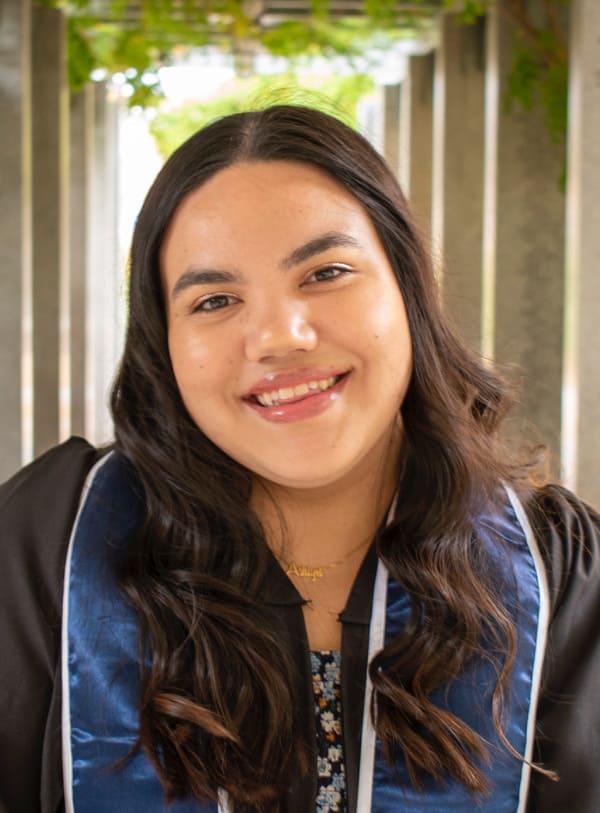 A portrait shot of Ashlyn Rodgers smiling while wearing a graduation robe and sash.