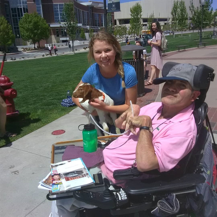 Two smiling students in front of the Knowledge Center. One is holding a goat.