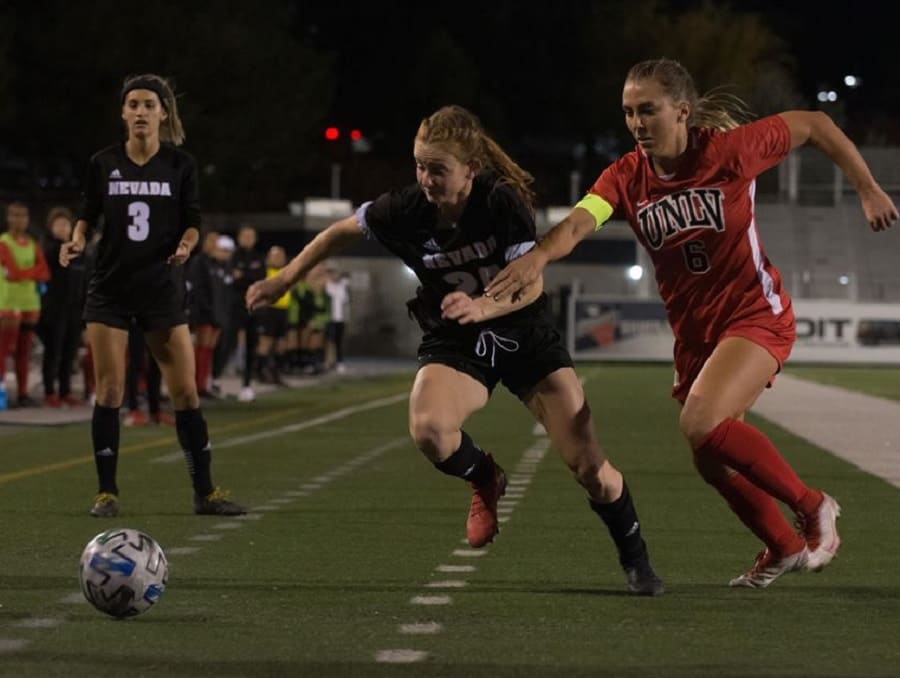 Emily rich on the soccer field during a game racing to keep control of the ball from the encroaching opposing team member