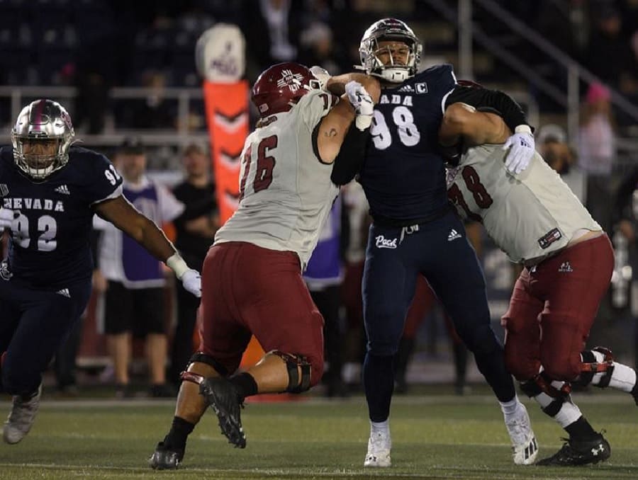 Sam Hammond on the football field during a game taking on two of the opposing team's players trying to tackle him